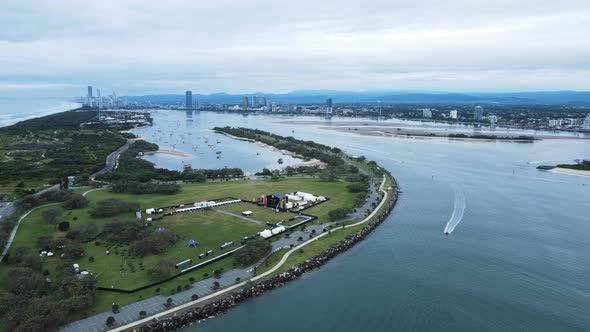 Music festival infrastructure set up in a coastal parkland close to a major city with towering high-