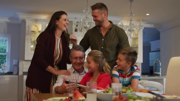 Caucasian parents, son, daughter and their grandfather sitting at table talking after family meal