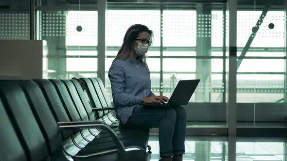 A Woman in a Safety Mask Is Operating a Laptop at the Airport