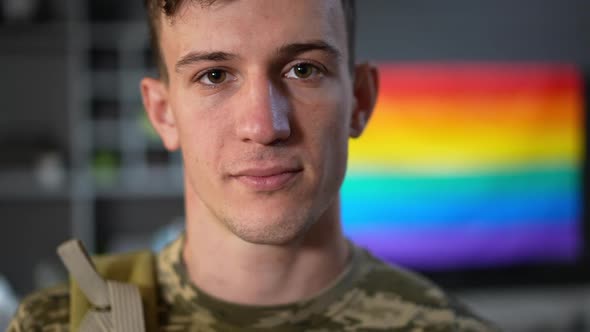 Headshot Portrait of Gay Soldier Posing Indoors with Rainbow Flag at Background