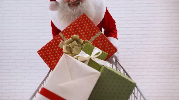 Senior Santa Claus Pushing Shopping Cart Full of Gift Boxes