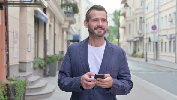 Man Checking Phone While Walking on Beautiful Street