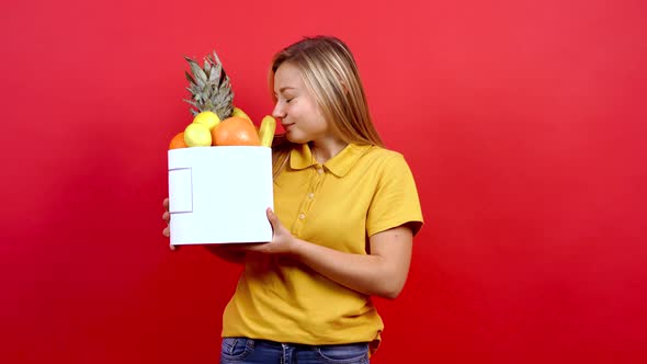 Cute and Slightly Fat Girl in a Yellow T-shirt Holding a Box of Fresh Fruit