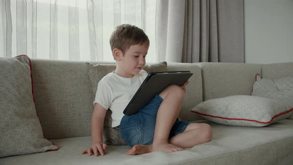 Cute Preschool Kid Boy Using Digital Tablet Technology Device Online Education Sitting on Couch at