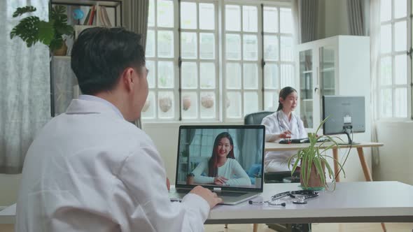 Asian Man Doctor Having Video Conference On Laptop In Workplace With Woman Patient On Screen Display