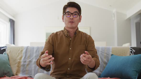 Asian man working at home, sitting on couch making video call, talking and gesturing