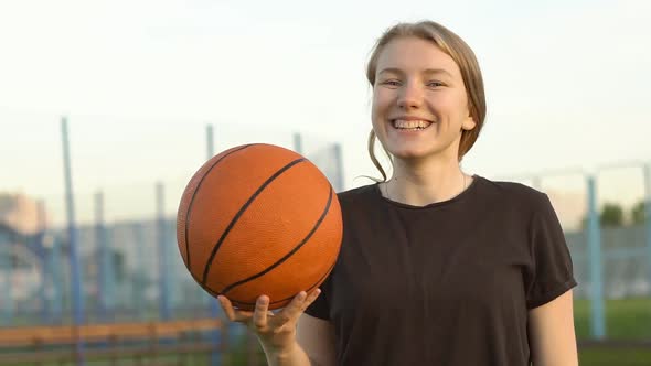 Young girl holding basketball ball looking positive and happy