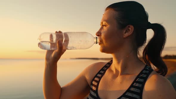 Portrait of a Tired Girl After a Workout Drinking Water From a Bottle at Sunset