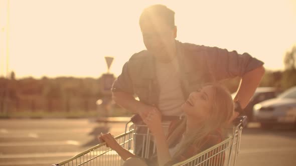 Couple Riding with Shopping Cart on the Parking Outdoors