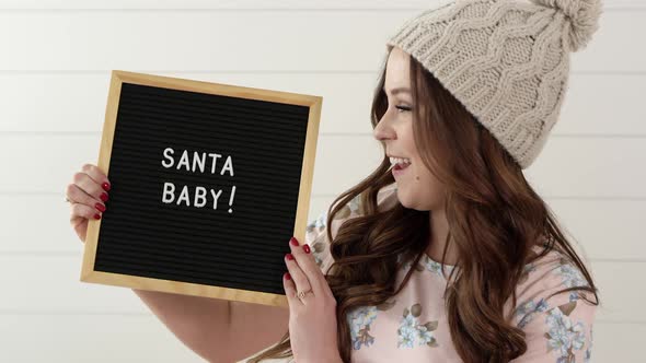 Woman smiling and holding sign that says, Santa Baby