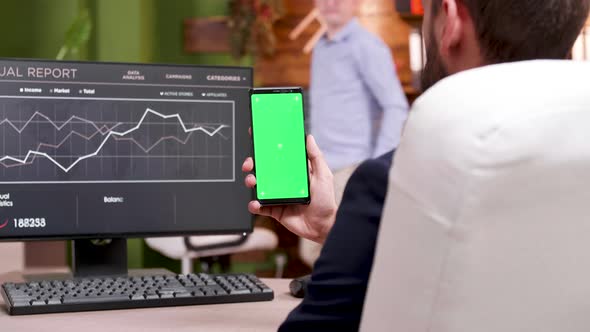 Businessman in Modern Workplace Holding Phone with Green Screen