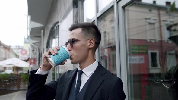 Man in Suit with Sunglasses Drinks a Cup of Coffee Turns and Looks Into Camera