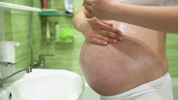 Pregnant Girl Lubricates Stomach with Cream Against Stretch Marks in the Bathroom