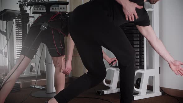 Young Woman in an EMS Costume Training with Exercise Equipment with Help of Her Coach