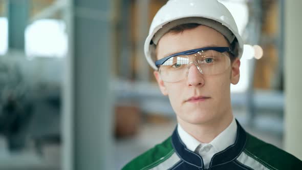 Young Engineer Wearing Protective Helmet Posing Looking at Camera at Modern Factory