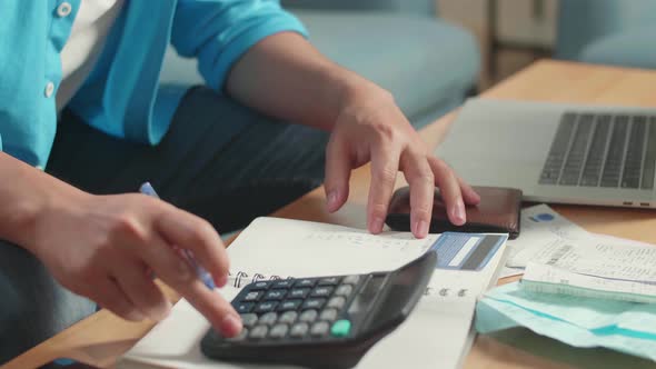 Man's Hand With Bill And Credit Card Calculating Money By Calculator Before Record In The Notebook