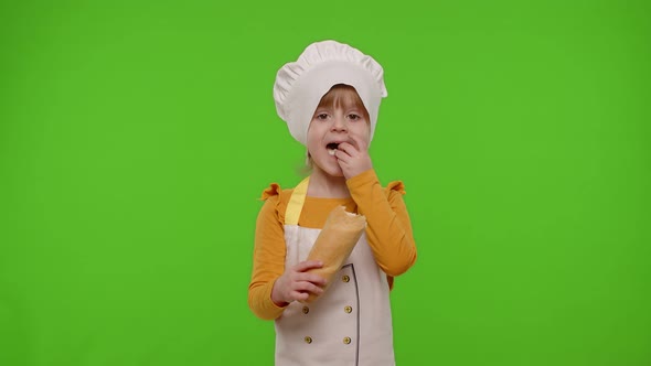 Child Girl Kid Dressed in Apron and Hat Like Chef Cook Eating Fresh Tasty Baguette Making Faces