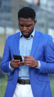 African American Man Looks on Phone with Angry Expression