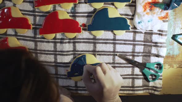 Woman decorates homemade vehicle shaped cookies with sugar icing. over head static shot 4K