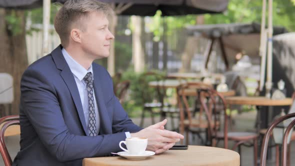 Pensive Businessman Sitting in Outdoor Cafe