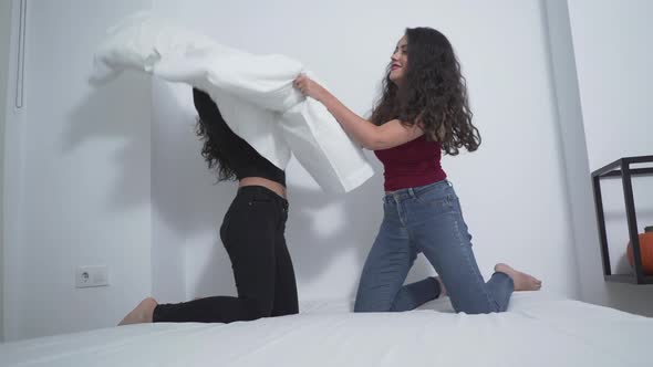 Two Women Laughing While Pillow Fighting On The Bed