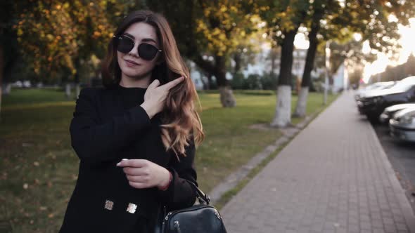A Spectacular Young Girl in a Stylish Black Outfit and with Sunglasses on Her Head Goes Along a City