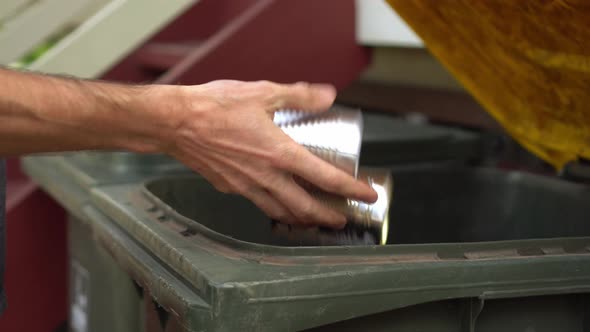 Person puts tin cans in recycle bin with yellow lid, closeup