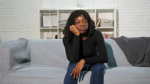 Bored Black Girl Sits on Grey Sofa Against White Wall Slow