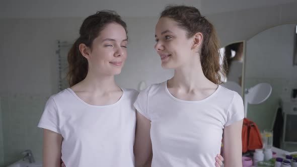 Front View Two Beautiful Identical Twins Looking at Each Other Turning to Camera Smiling Putting