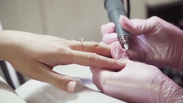 Manicure procedure close-up. Girl manicurist in pink medical gloves and a special device