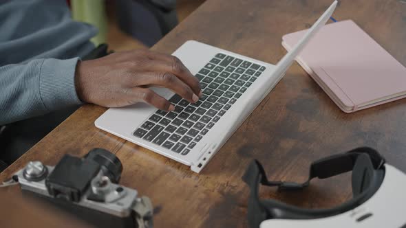 Dark Wood Working Desk Man Typing on Computer Laptop Keyboard with Notebook VR Headset and Coffe Cup