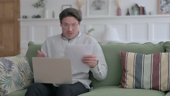 Man with Laptop Reacting to Loss on Documents, Sofa