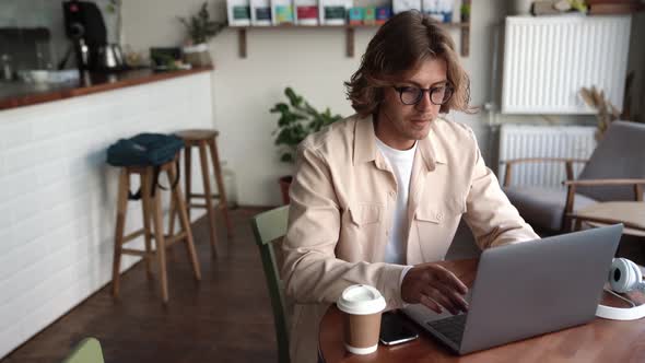 Serious blond man in eyeglasses working on laptop