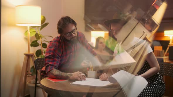 Two Stylish Diverse People Are Sitting At The Table While Energetically Discussing the Project