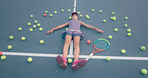 Girl Laying on the Tennis Court Surrounded By Balls and Paddle