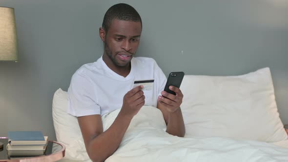 Online Payment Success on Smartphone By African Man in Bed 