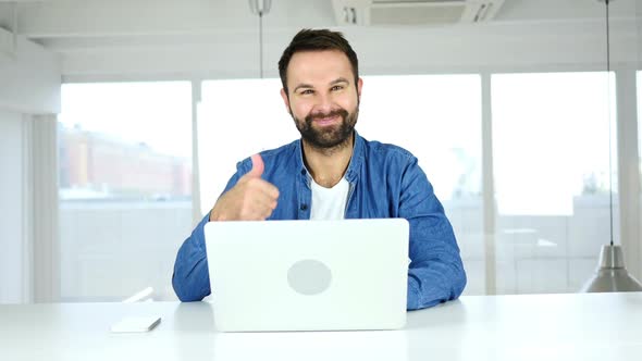 Thumbs Up By Man Sitting in Office Looking at Camera