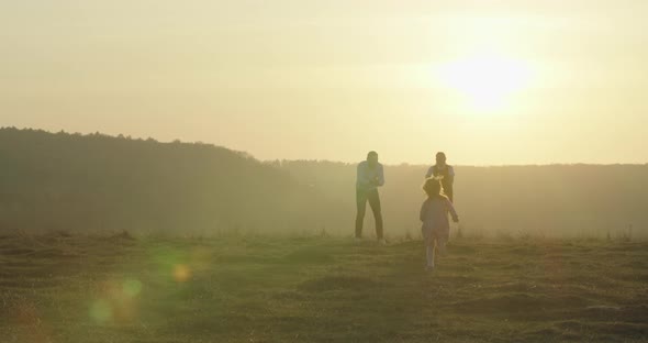 Happy Young Family Is Walking in the Field. A Little Girl Is Running To Her Parents. 