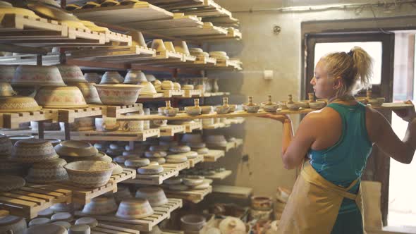 Female Pottery Artist Aranging Clay Dishware on Wooden Rack Shelves