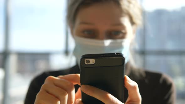 Woman in Mask with Phone in Hands Sits in Shopping Center on Sunny Day, Coronovirus Quarantined