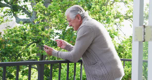 Side view of senior man leaning on railing while using smart phone in balcony