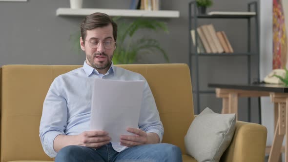 Young Man Reading Papers Loudly on Sofa