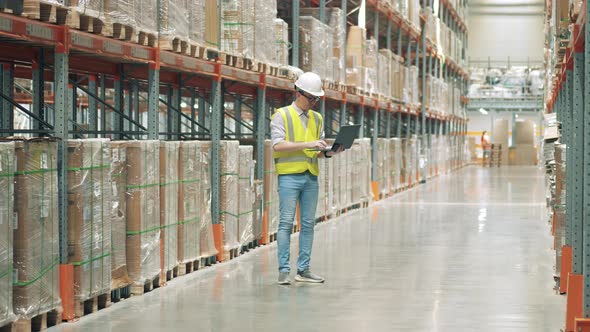 Male Employee with a Laptop is Doing Inventory in the Storehouse