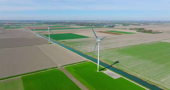 Wind turbines spinning and generating clean energy in Holland, with classic water canal crossing fla