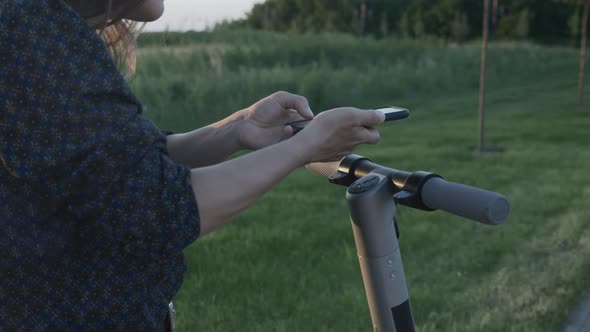 Woman takes electric scooter in parking split using mobile phone application.