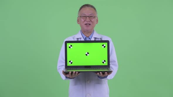 Happy Mature Japanese Man Doctor Talking While Showing Laptop