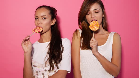 Closeup portrait of two young sexy girls eating lollipop
