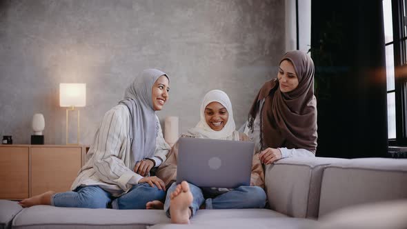 Three Muslim Girls Look at the Laptop Sitting on the Couch Smiling and Laughing