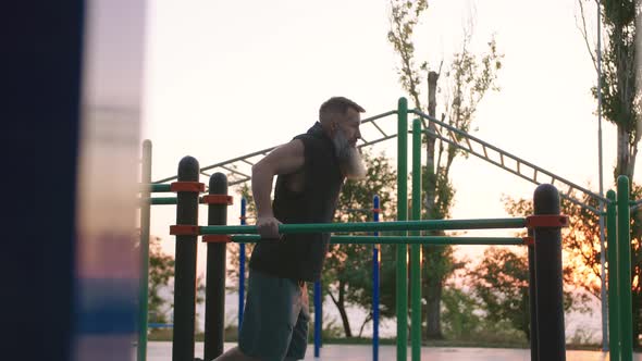 Fit Handsome Middle Aged Man with Long Gray Beard Doing Push Ups on Parallel Bars on Sports Ground