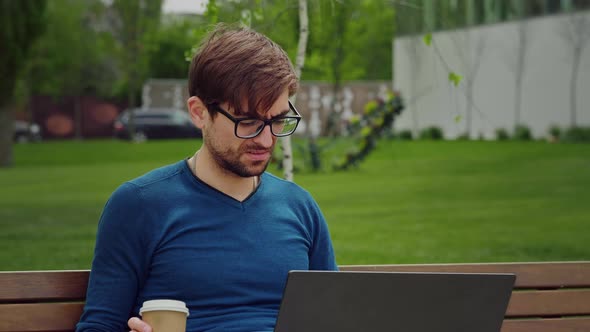 Man works on his laptop while sat on a bench outdoors slow motion